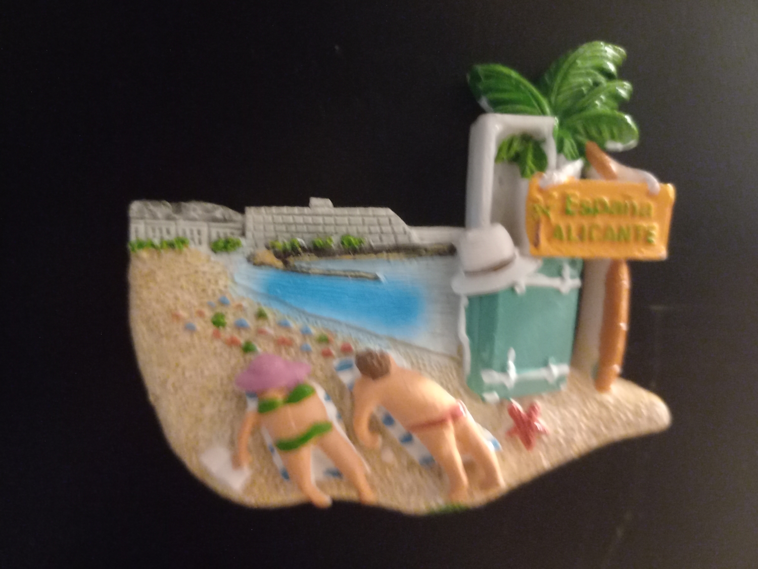 Plażowicze w Alicante przedstawieni są tak, jakby przejechał po nich ciężki pojazd z gąsienicą. Bardzo elegancka budka do przebierania z nieproporcjonalnie dużym kapeluszem dopełnia kompozycjię